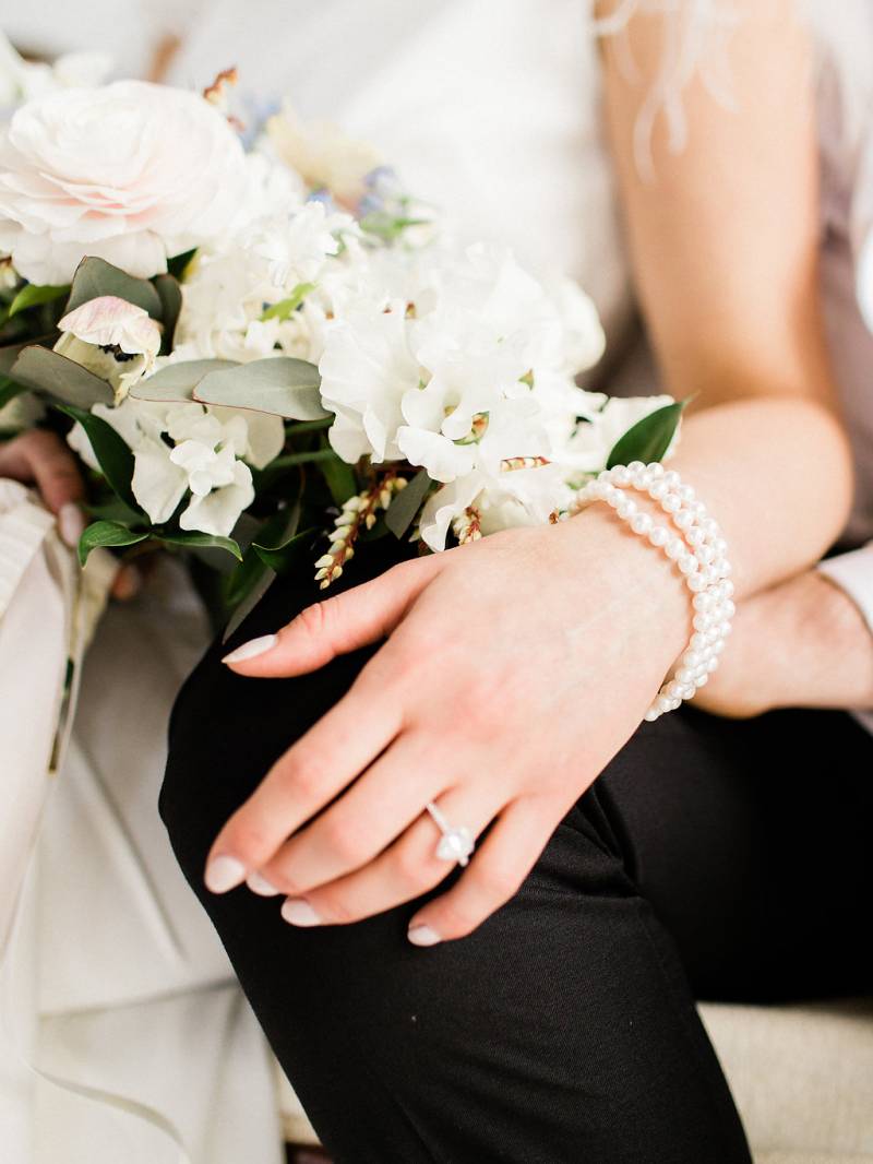 Woman with engagement ring and pearl bracelet hang beside white bouquet 