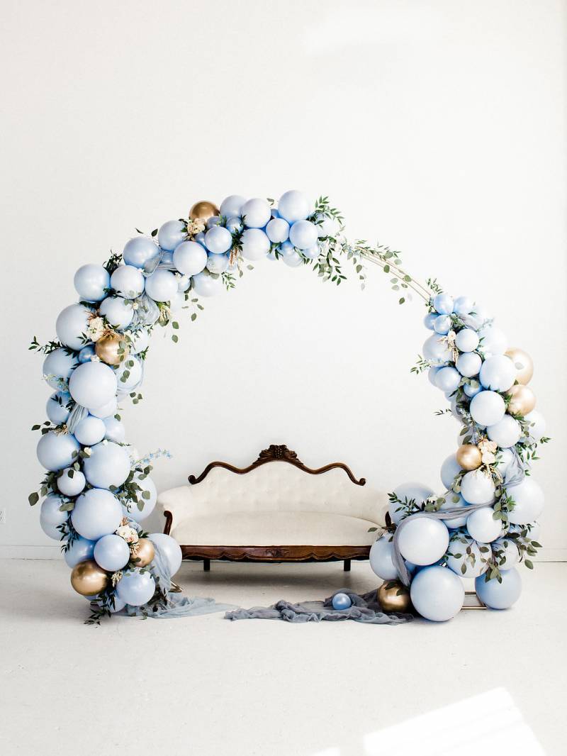 Powder blue balloon wedding arch with gold balloon accent in front of white bench 