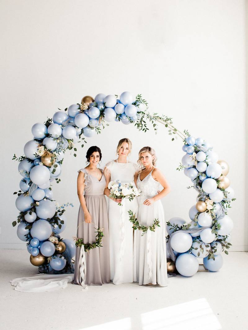 Three woman standing under powder blue balloon wedding arch with gold accents