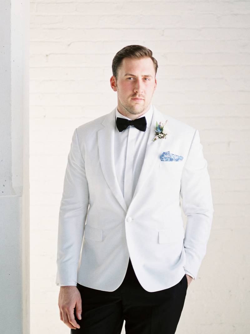 Man in white suit jacket and black tie stands with hand in pocket