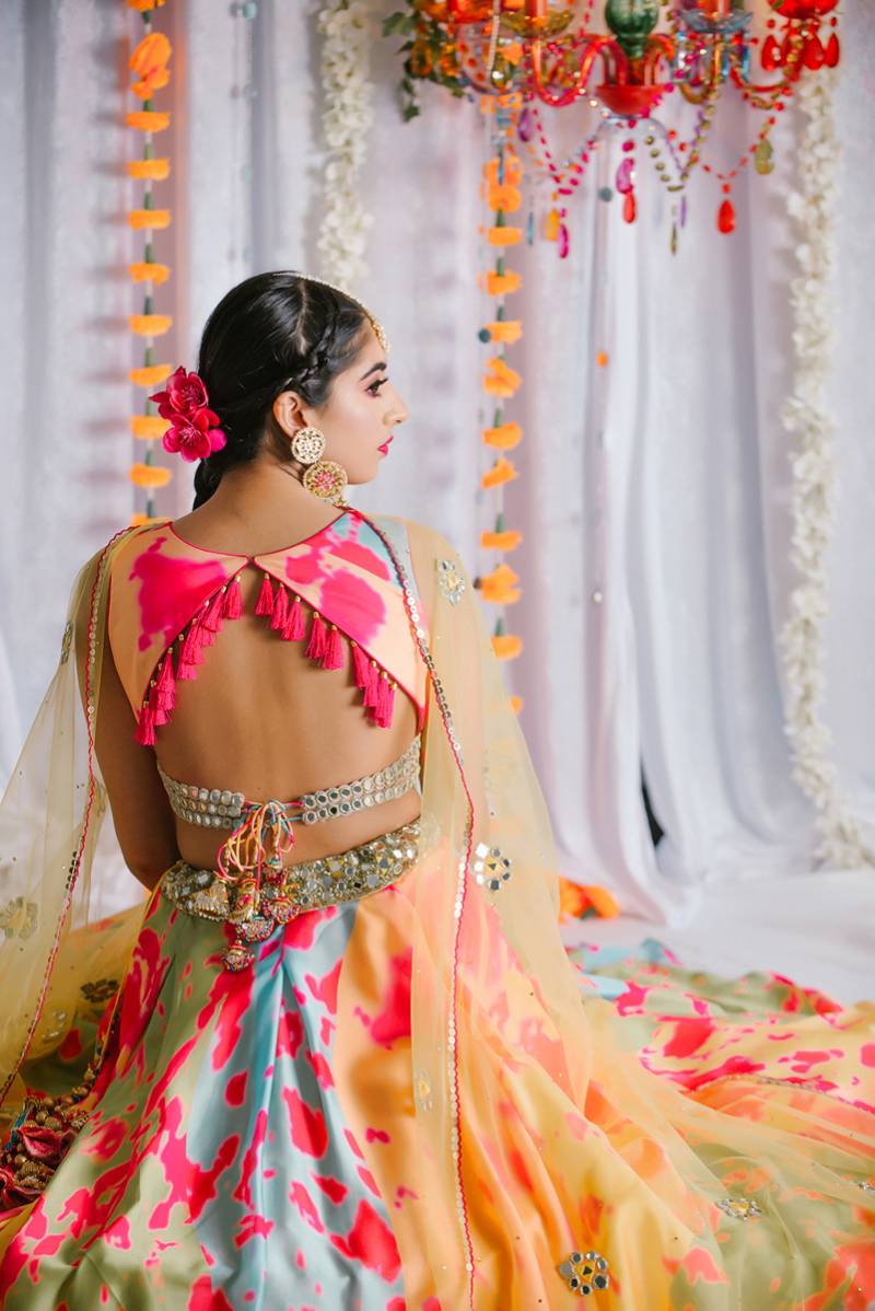 Woman in pink orange and yellow dress and yellow veil sits in front of flower wall