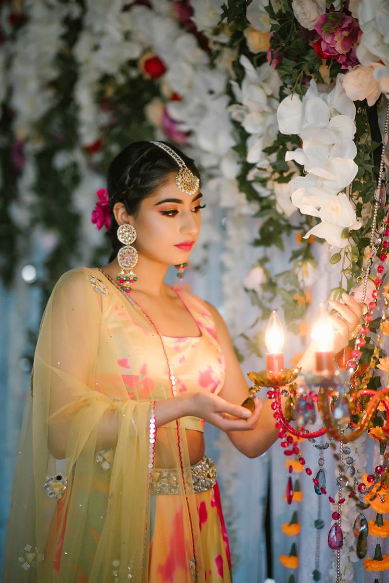 Woman in colorful dress and yellow veil looks at hanging lights on flower wall