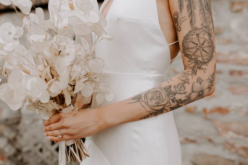 Torso of woman in white dress and tattooed arm holding clear white bouquet 