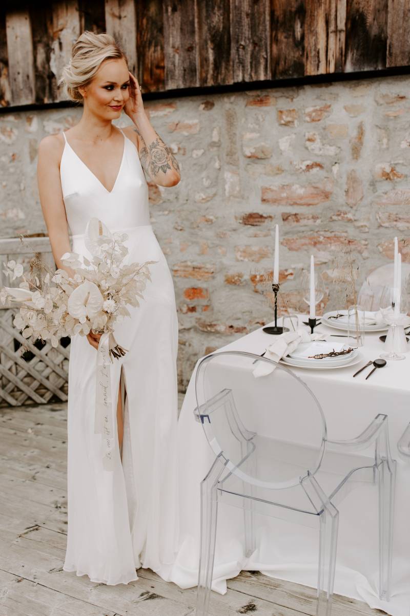 Woman in white dress holding clear white bouquet beside white minimalist table