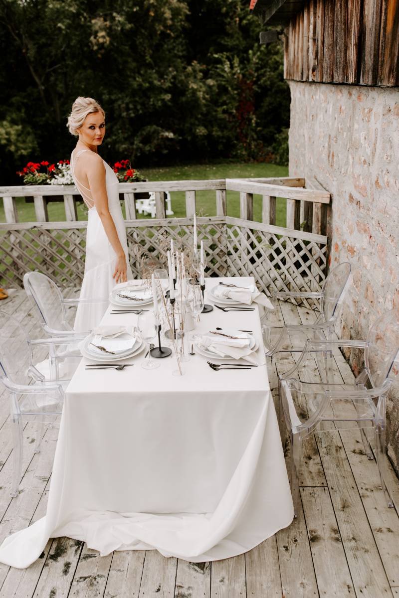 Woman in white backless dress facing at white minimalist table on wooden deck 