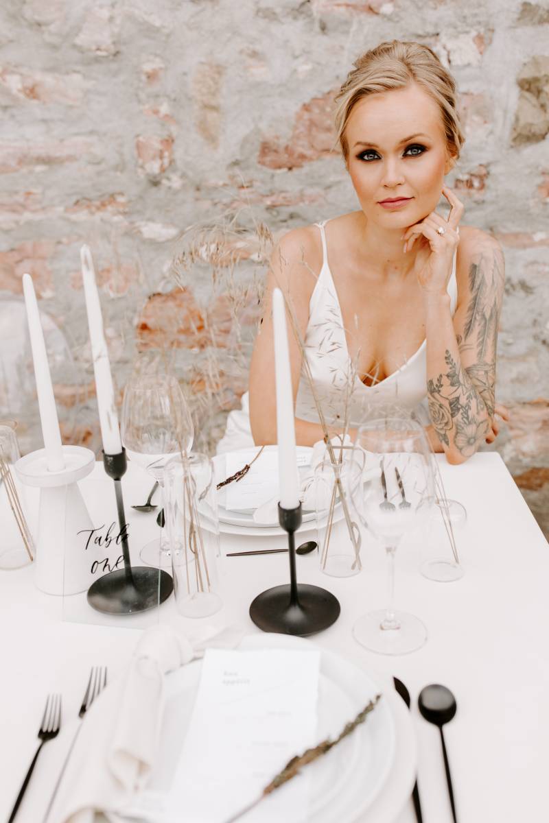 Woman leans on tattoo covered arm sitting at white minimalist table with black cutlery