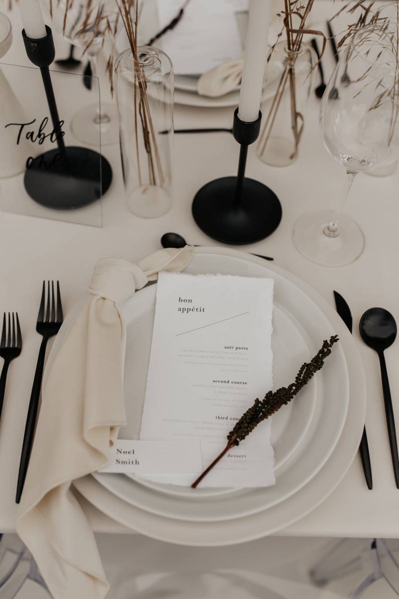 Minimalist Stationery place setting on white table with black cutlery and taper candles