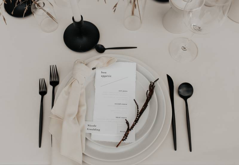 Stationery place setting on white table with black cutlery 