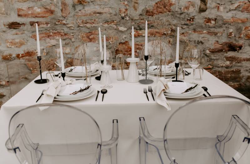 Minimalist white table setting with black cutlery and clear chairs 