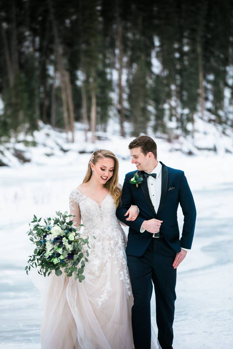 Bride and groom walk together in arms smiling on frozen forest tundra 