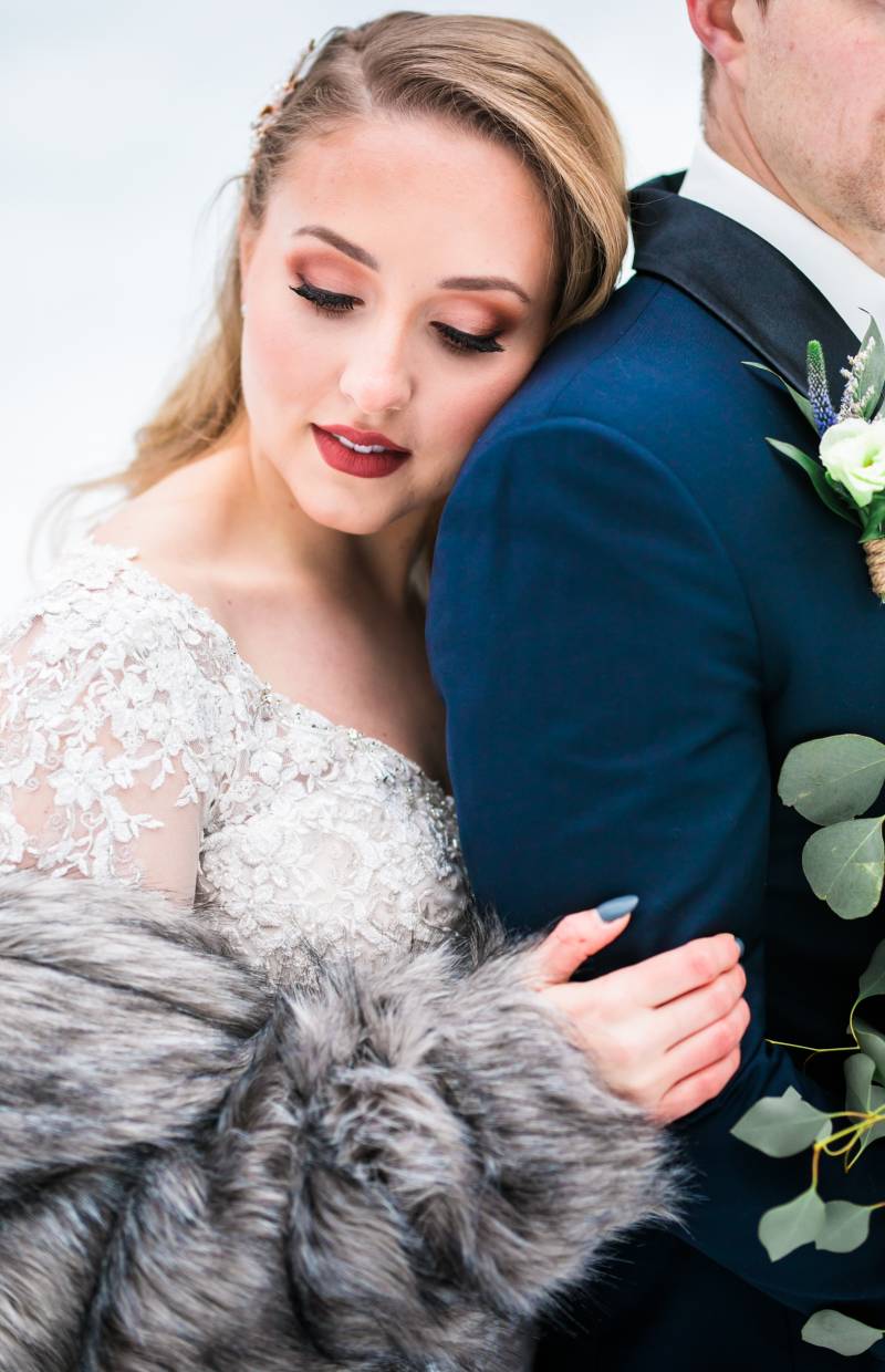 Bride leans on grooms back waring grey fur overcoat 