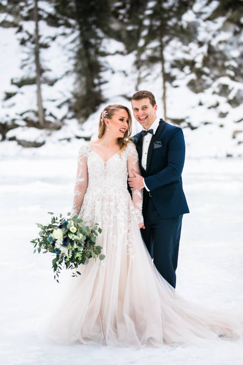 Groom holds bride from behind smiling on snowy tundra