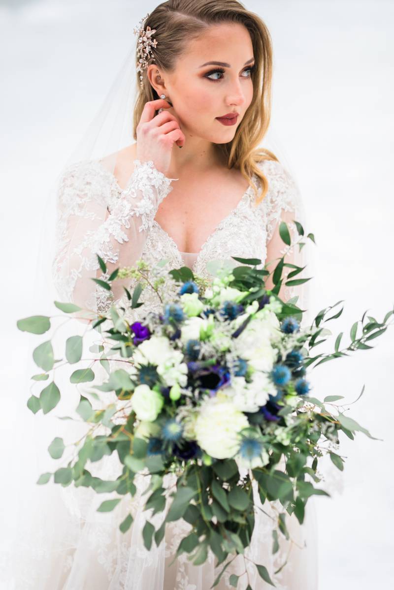 Bride in white lace sleeved dress holding white blue and cobalt bouquet 
