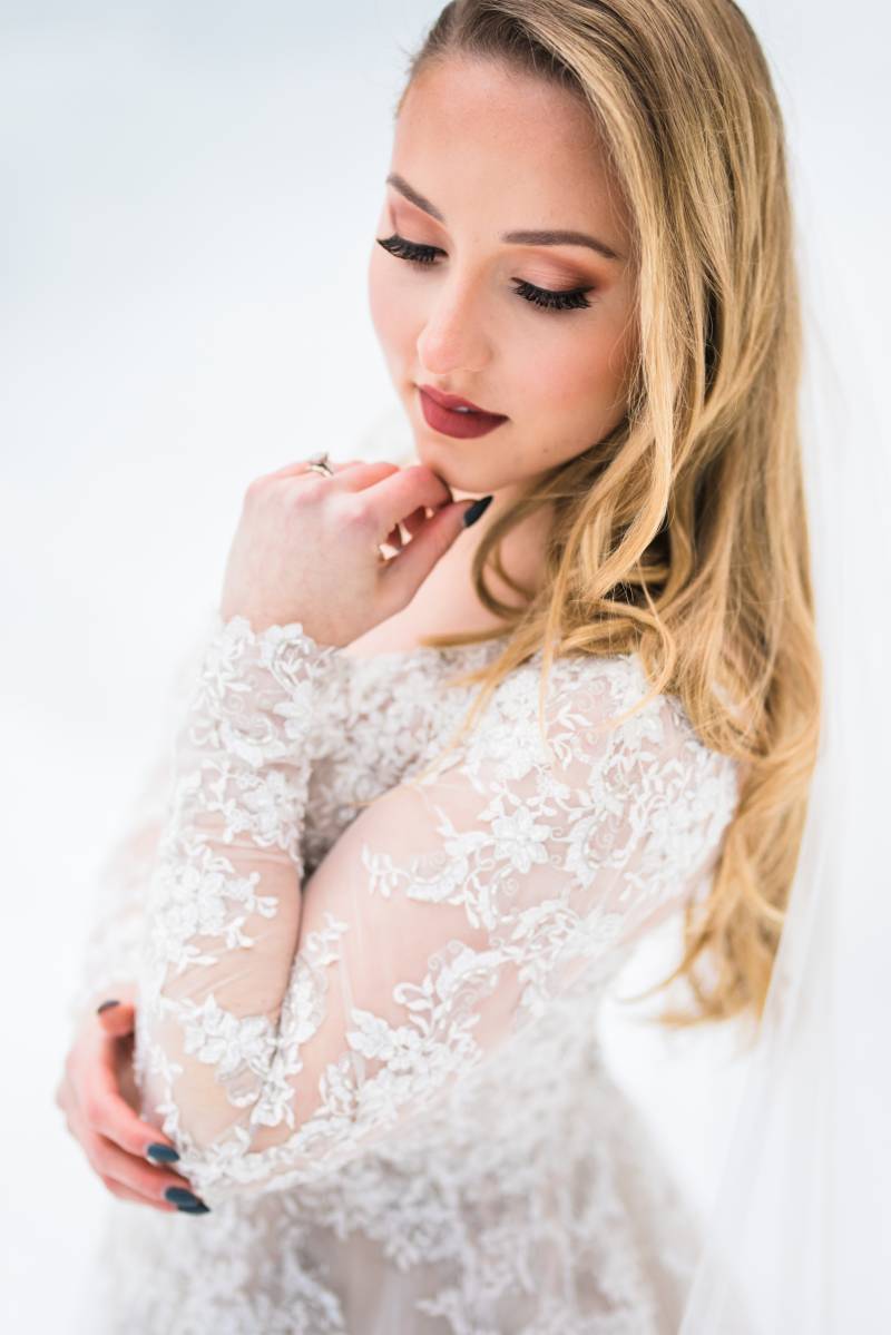 Bride in white lace dress touches chin 