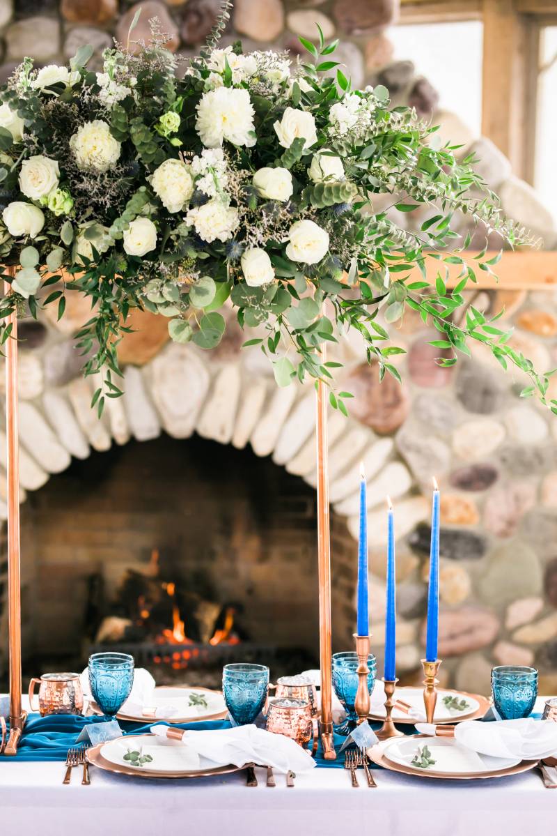 Cobalt candlesticks on top of blue table runner and bronze place settings in front of stone fireplace 