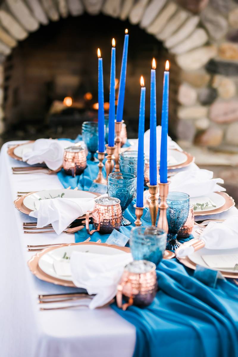 Cobalt candlesticks on top of blue table runner and bronze place settings 