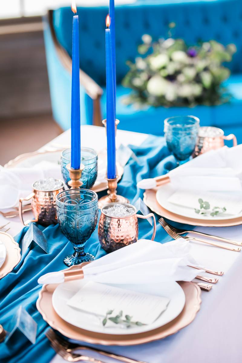 Cobalt candlesticks on top of blue table runner and bronze place settings 