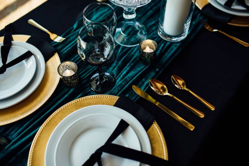 Table setting with gold cutlery on black table with turquoise table runner  