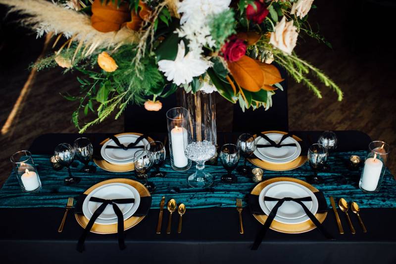 Large orange white and red floral centerpiece on black table with gold cutlery and teal table runner 
