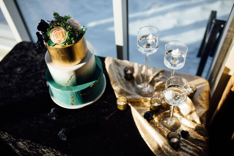 Teal white and gold wedding cake on  black table with gold table runner 