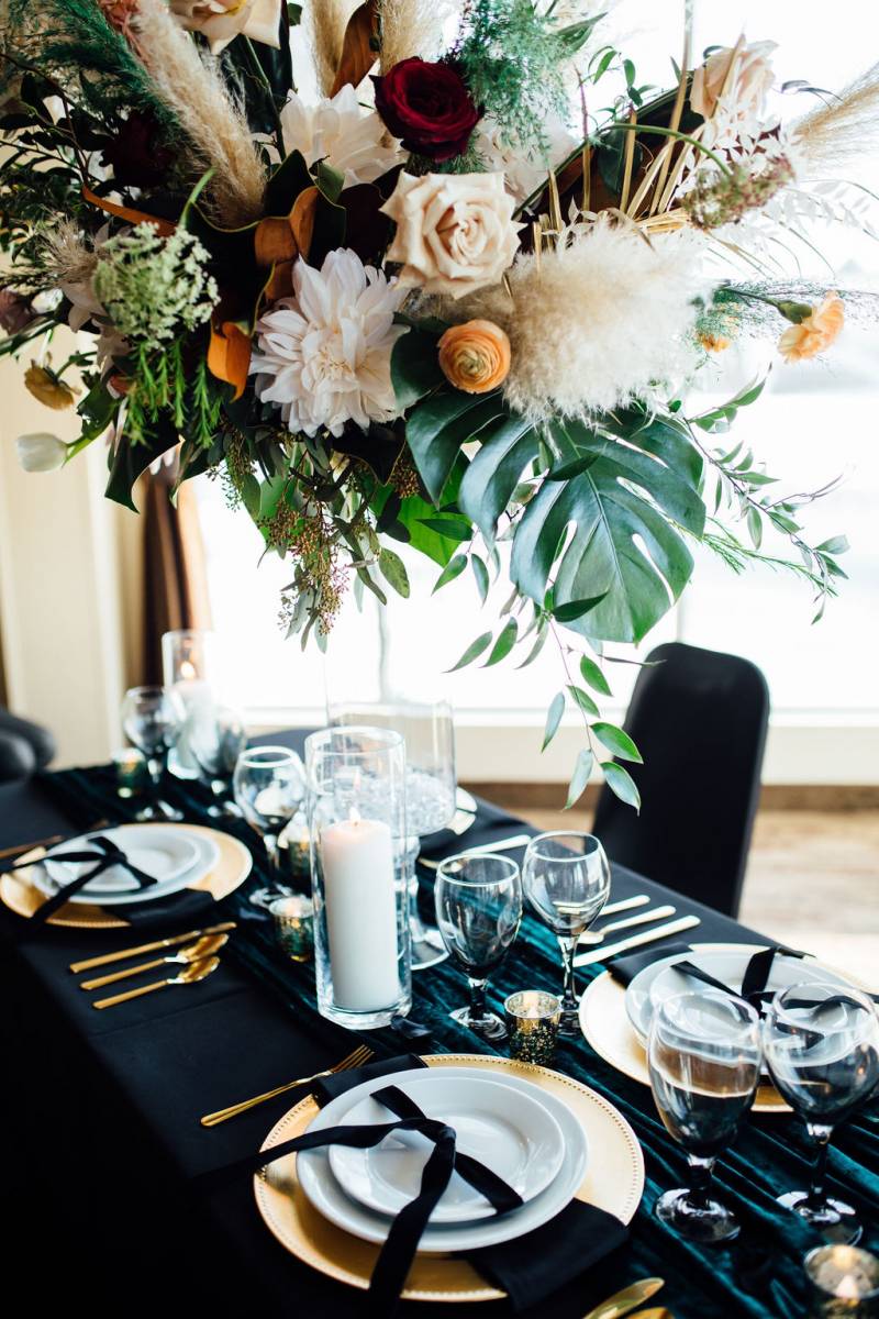 Large orange white and red floral centerpiece on black table with gold cutlery and teal table runner 