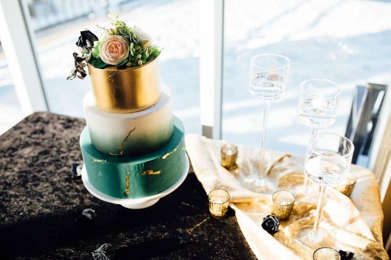 Teal white and gold wedding cake on black table with gold table runner 