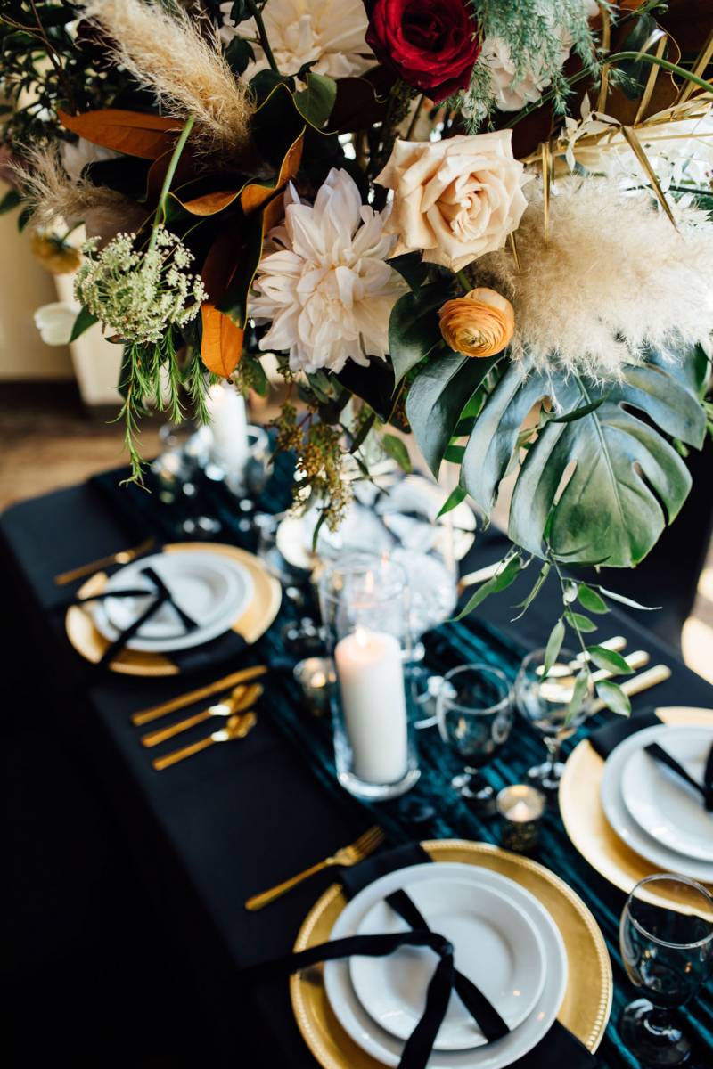 Large orange white and red floral centerpiece on black table with gold cutlery and teal table runner 