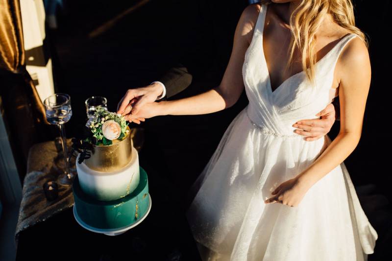 Man and woman cut teal white and gold wedding cake white embracing 