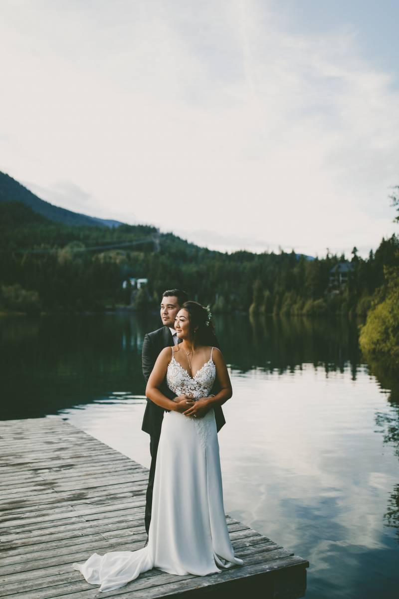 Bride and groom embrace at the edge of dock looking towards pond 
