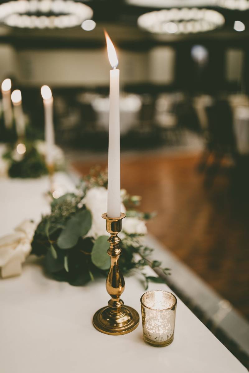 Gold candlestick lit beside small  candle in clear glass 
