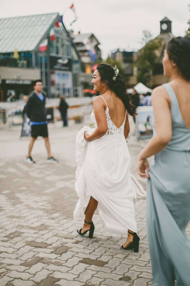 Bride smiling holding dress up while walking on brick sidewalk 