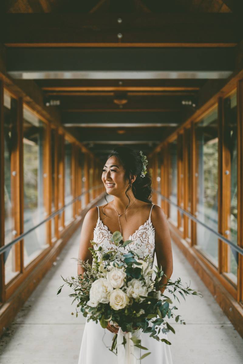 Bride smiling holding white bouquet  in white lace dress in hallway 