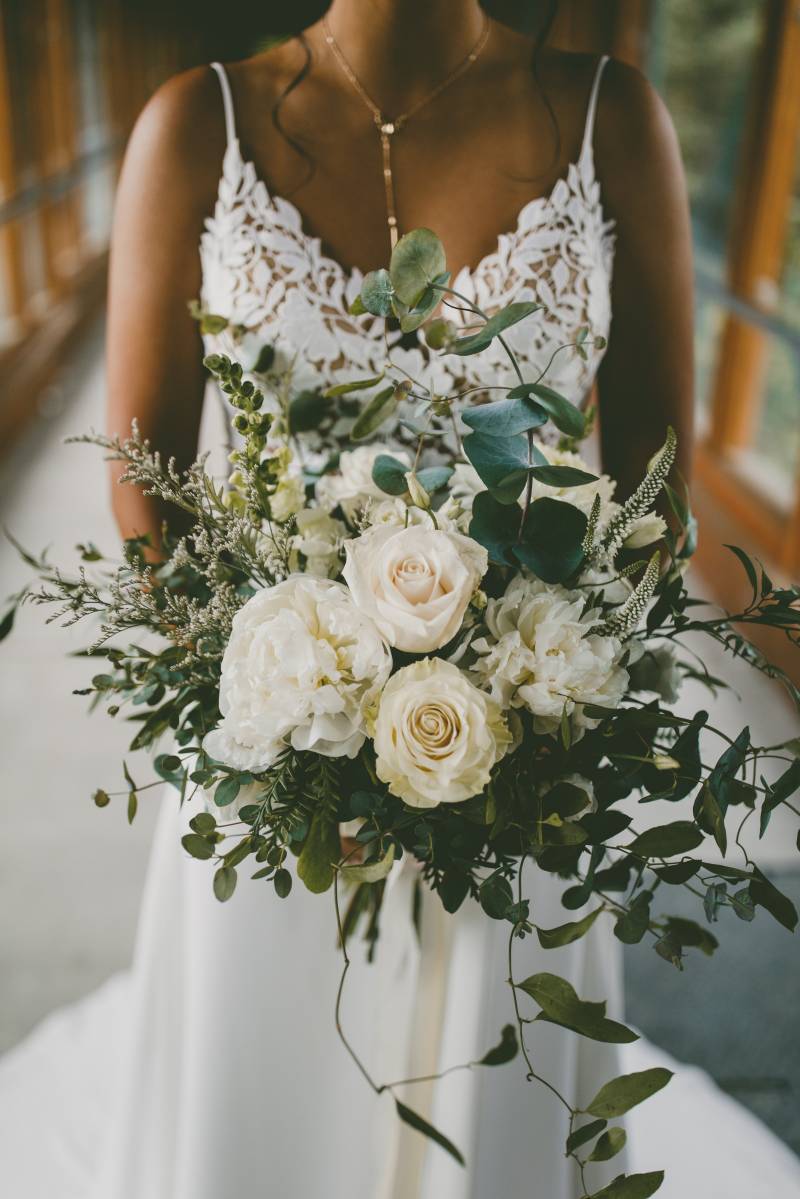 Bride holds out white bouquet in white lace dress 