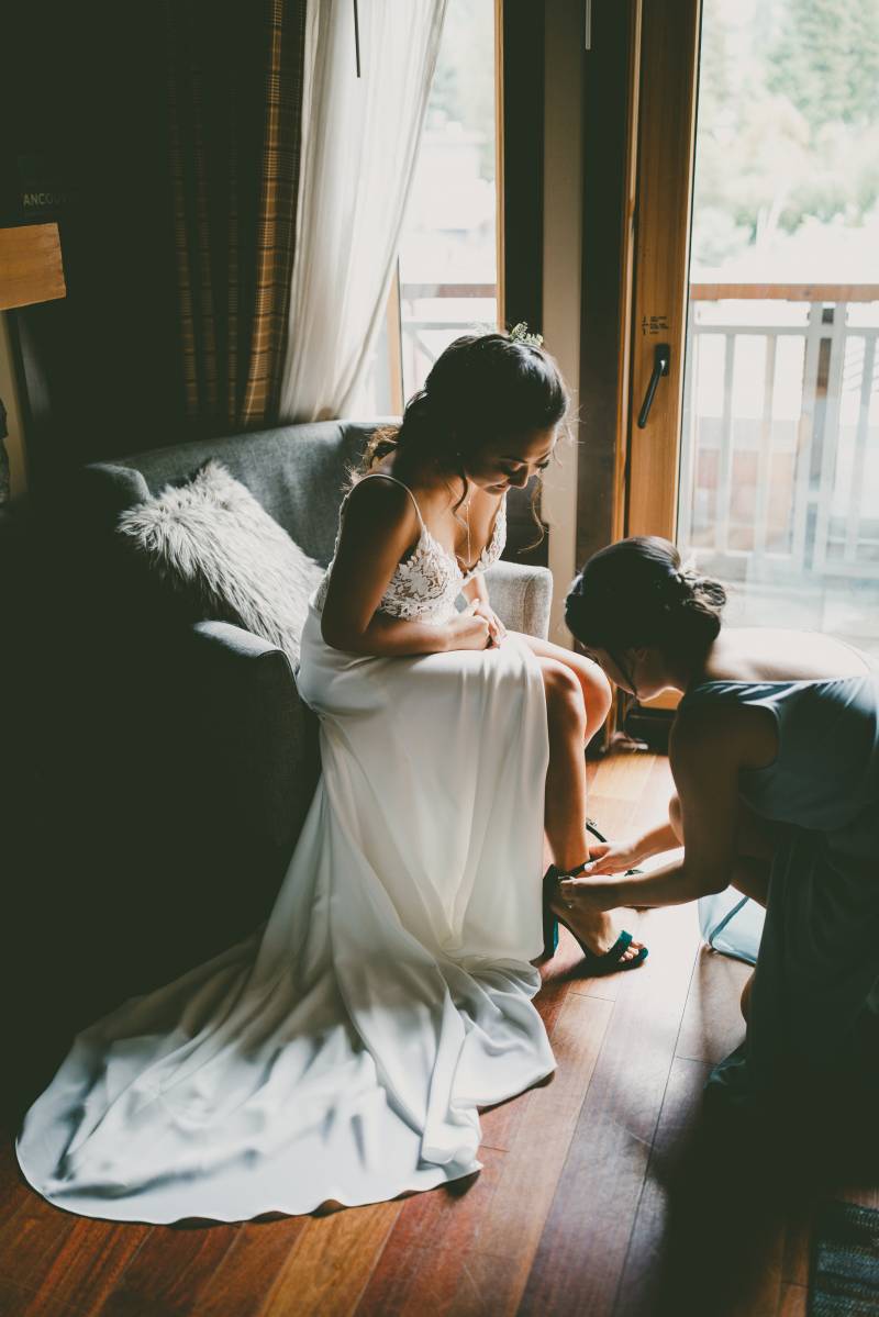 Woman adjusts brides heels sitting in large white dress 