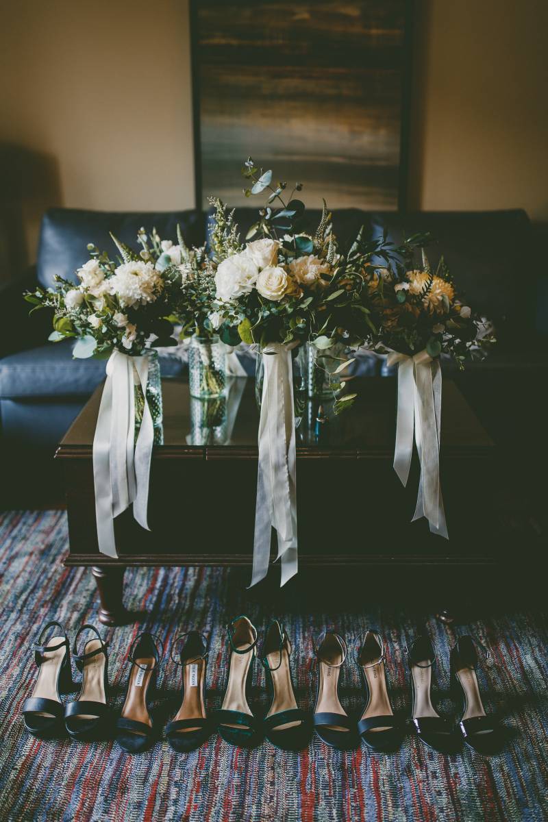 White Bouquets with white ribbons on table behind black heels 