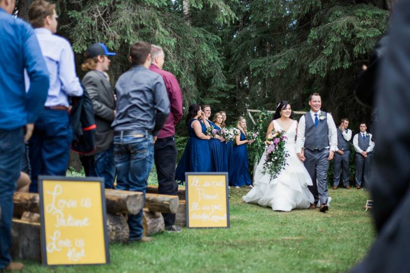 Bride and groom walk together down aisle holding bouquet with yellow signs 