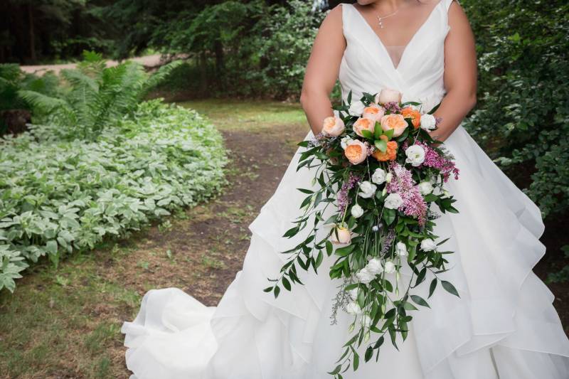 Bride in white dress holding bouquet in front of lush green foliage 
