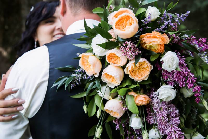 Bride and groom embrace holding yellow white and purple bouquet