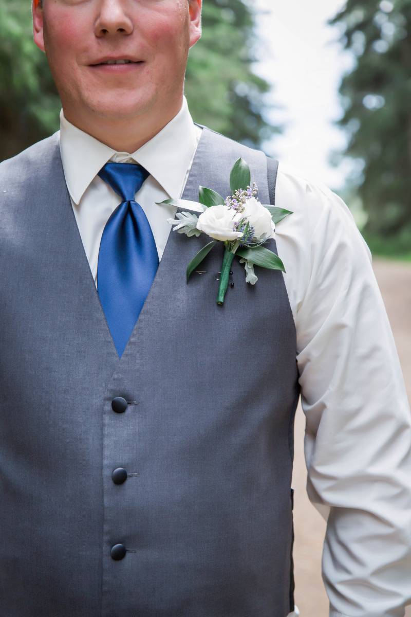 White boutonniere on chest of groom wearing pale blue grey vest  