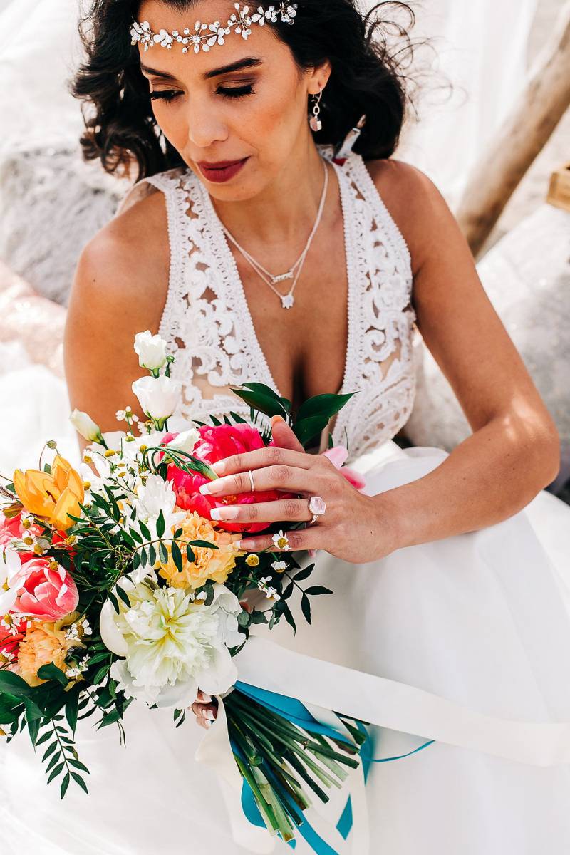 Bride in white lace dress caresses pink yellow and white bouquet 