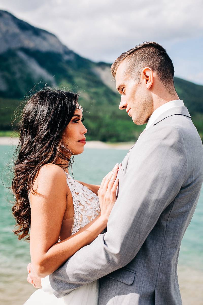 Man and woman embrace in front of lake and mountains 
