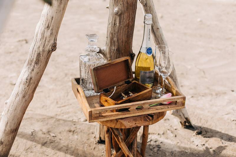 Small wooden tray with box and bottle of wine with glasses sitting on small wooden stool 