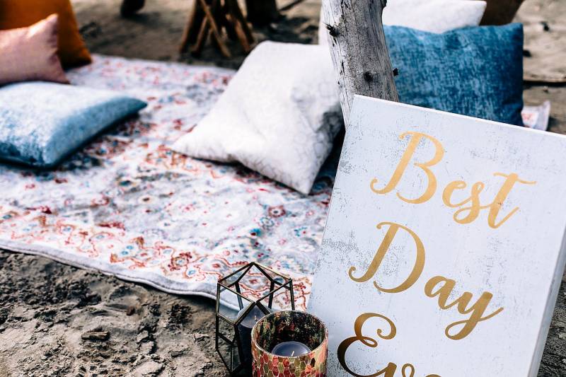 White sign with gold lettering beside carpet with pillows and candles 