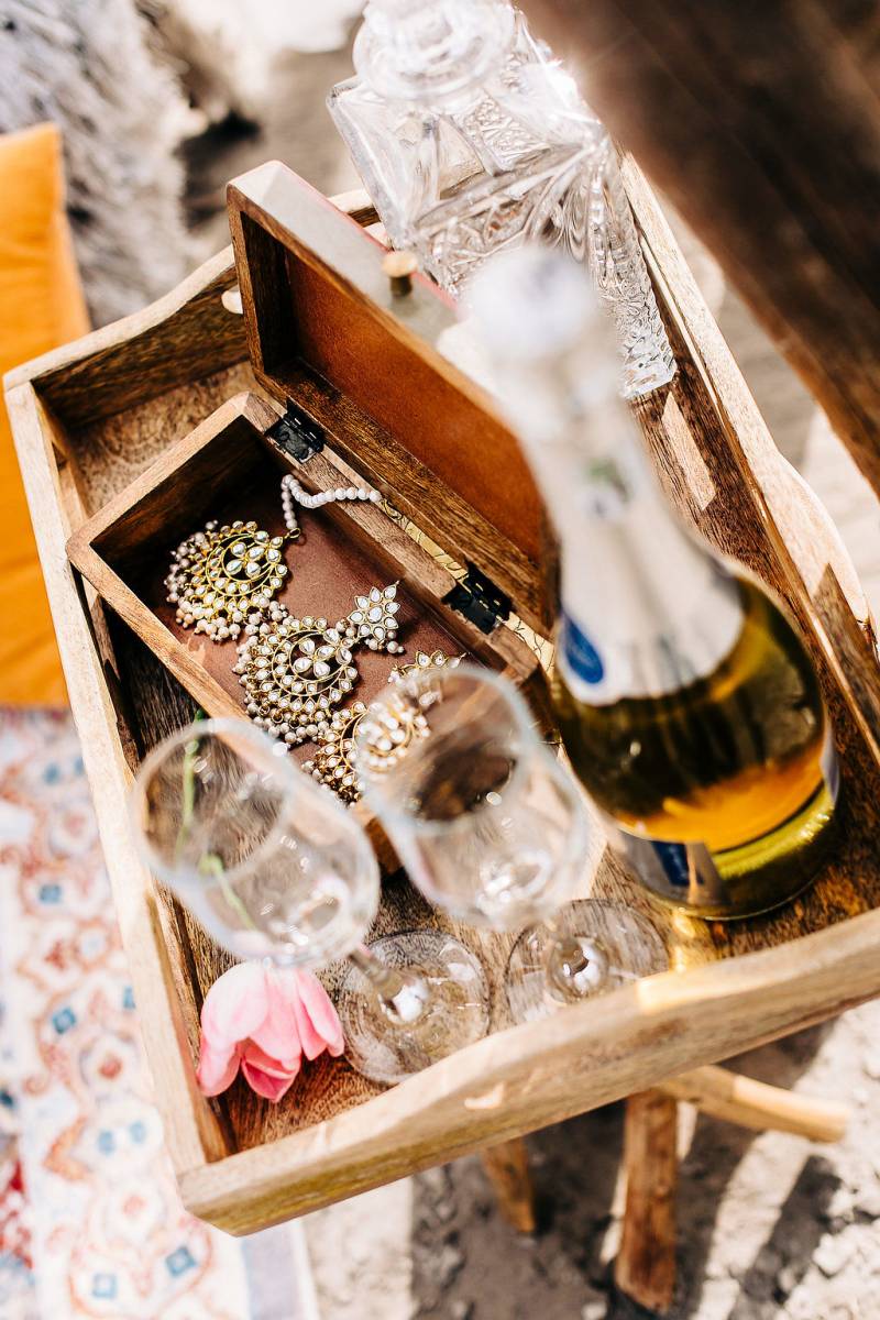 Small wooden tray with box and bottle of wine with glasses sitting on small wooden stool 