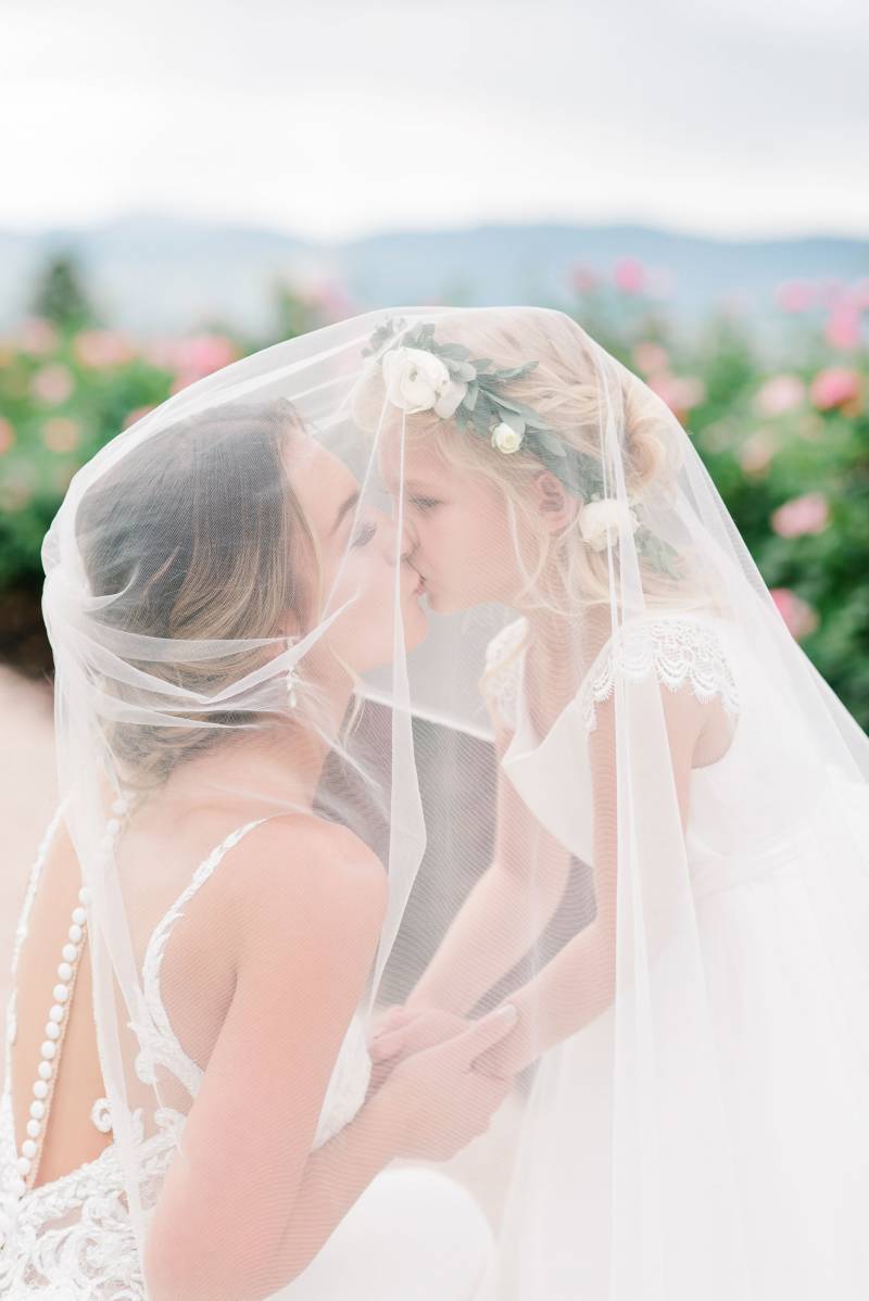 Bride kissing child underneath white veil  
