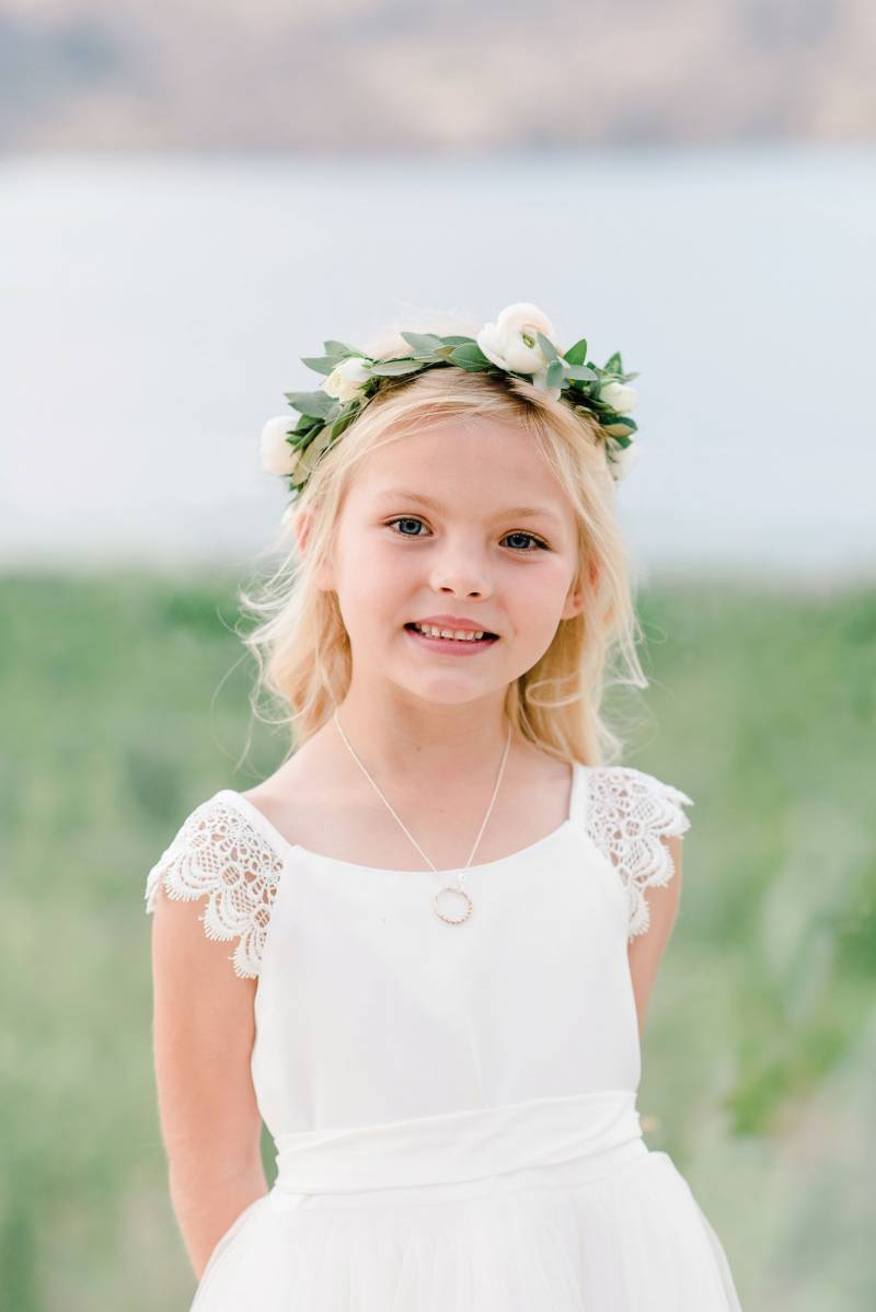 Child in white dress and white flower crown smiling 
