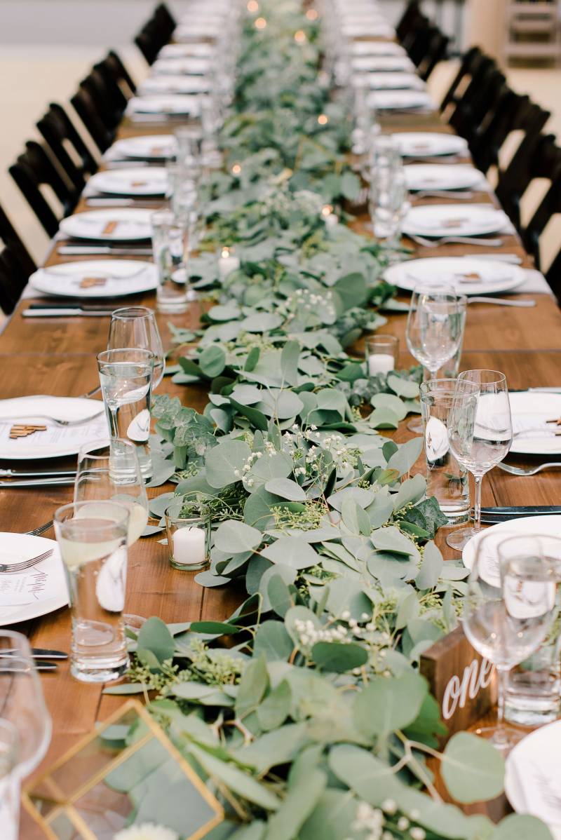 Long green table runner along length of wood table surrounded by wooden chairs 