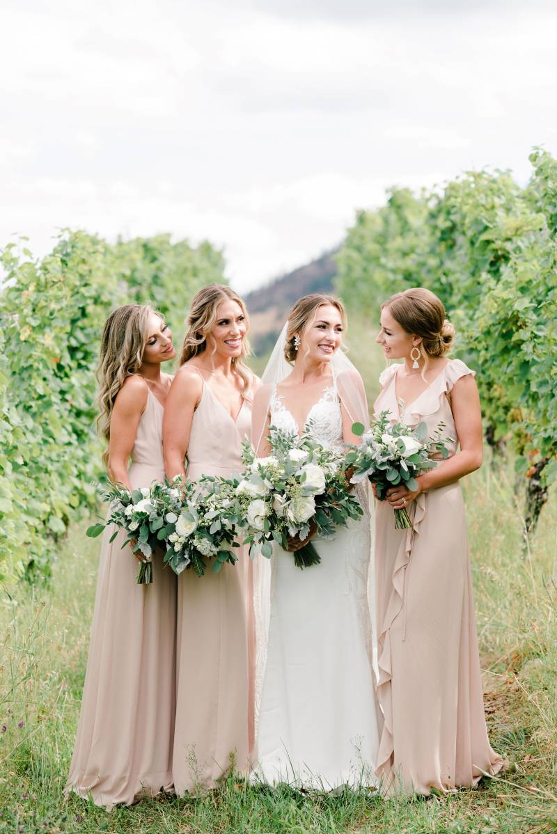 Bride smiling at bridesmaids holding white bouquets in peach field