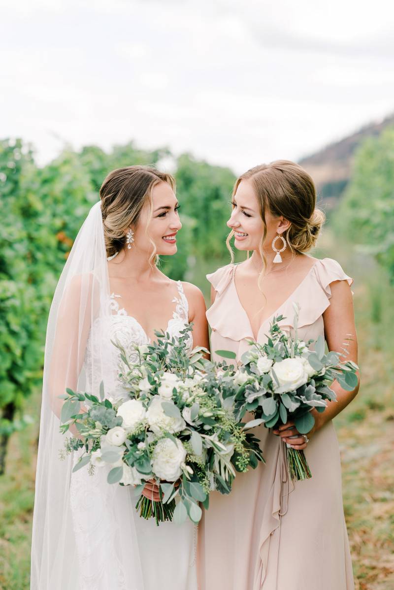 Bride looks at smiling beside bridesmaid holding white bouquet 