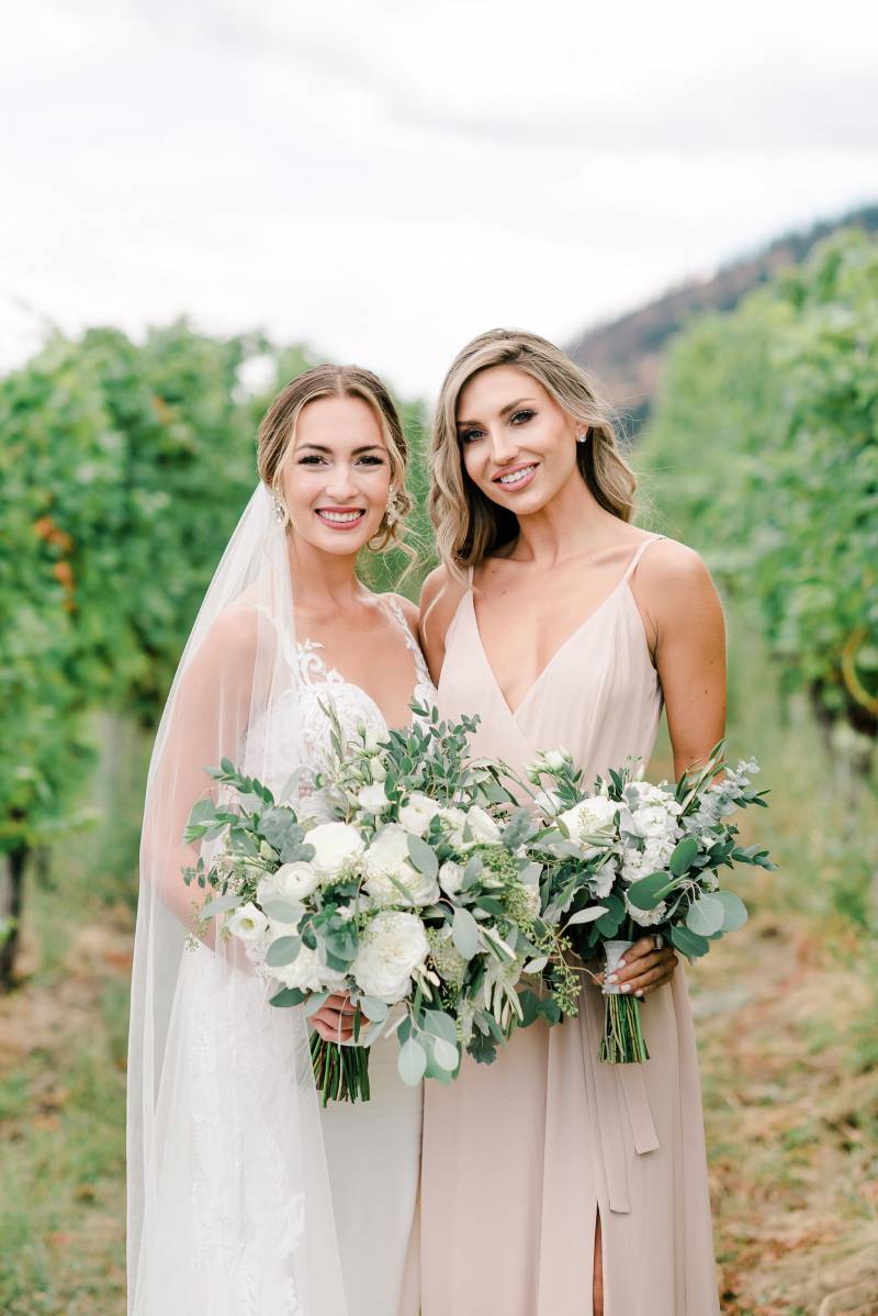 Bride smiling beside bridesmaid holding white bouquet 